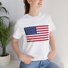 Welcome to our shop, where patriotism meets style! Introducing our exclusive white t-shirt featuring a bold American flag print on the front, designed to make you stand out with pride. Crafted exclusively with Bella + Canvas 3001, known for their lightweight, flowy, and comfortable fit, our t-shirt offers the perfect blend of style and comfort. Each shirt is meticulously crafted to order, ensuring a fresh print tailored just for you. While we strive for perfection, we understand that sometimes issues may arise. Therefore, we regret to inform you that refunds or exchanges are not available due to the personalized nature of our products. However, your satisfaction is our priority, so please consult our sizing guide to select the perfect fit for you. Please note that slight color variations m American Flag T-shirt For 4th Of July, Cotton Crew Neck T-shirt With Flag Print, White Americana Letter Print T-shirt, Americana Cotton T-shirt With Letter Print, White American Flag T-shirt For Independence Day, White T-shirt With American Flag For Independence Day, White Cotton T-shirt With American Flag Print, American Style Cotton T-shirt With Short Sleeves, Patriotic Short Sleeve T-shirt With Flag Print