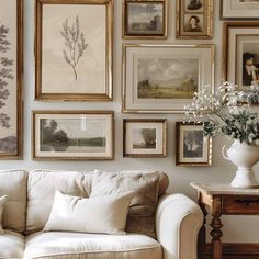 a living room filled with lots of framed pictures on the wall above a white couch