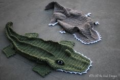 two knitted crocodiles laying on the ground next to each other, one is green and the other is gray