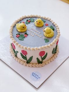 a birthday cake decorated with rubber ducks and flowers on a white tableclothed surface