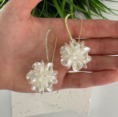 the hand is holding two white flower earrings