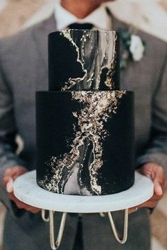 a man holding a black and gold wedding cake on top of a white platter