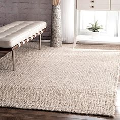 a white bench sitting on top of a wooden floor next to a rug and vase