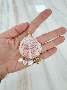 a person's hand holding a pink shell with pearls and heart charms on it