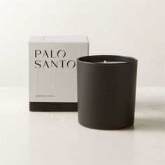 a black candle sitting next to a box on a white counter top with the words palo sano written in it