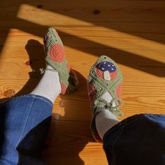 someone wearing crocheted shoes and jeans standing on a wooden floor