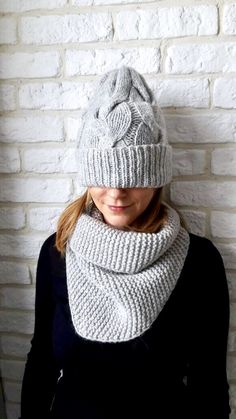 a woman wearing a knitted hat and scarf in front of a white brick wall