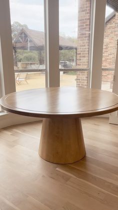 a round wooden table sitting in front of large windows on top of a hard wood floor