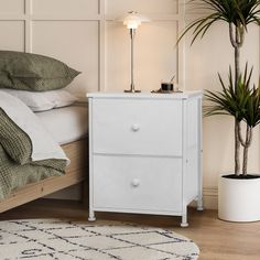 a white nightstand next to a bed with a plant on it and a potted plant in the corner