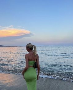 a woman in a green dress is standing on the beach looking out at the water