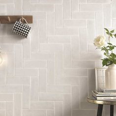 a white tiled wall with two mugs hanging on it's hooks next to a small table