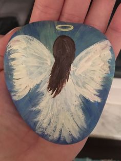 a hand holding a rock with an angel painted on it