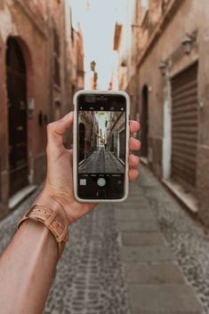 a hand holding up a cell phone taking a selfie on an alleyway with buildings in the background