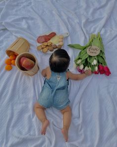 a baby is laying on a bed with fruits and vegetables