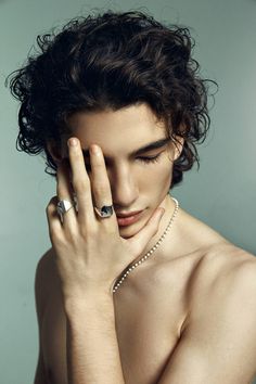 a shirtless young man with his hand on his face and wearing an unusual ring