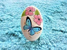 an easter egg decorated with flowers and a butterfly painted on the side, sitting on a blue carpet