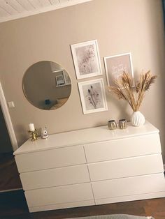 a white dresser with pictures on the wall and a mirror above it in a living room