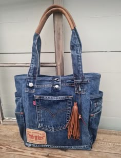 a blue jean purse with leather handles and tassels on the front, sitting on top of a wooden table