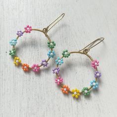 two pairs of colorful beaded hoop earrings on white wooden surface with small flowers in the middle