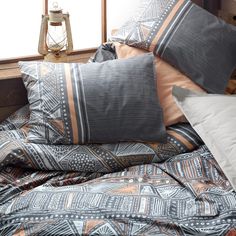 a bed covered in pillows and blankets next to a window with a lamp on it