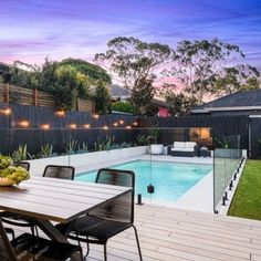 an outdoor dining table and chairs near a pool with lights on the fence around it