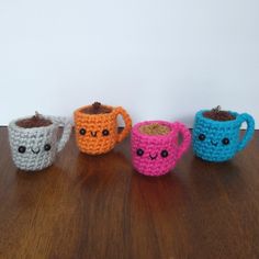 three crocheted coffee mugs sitting on top of a wooden table