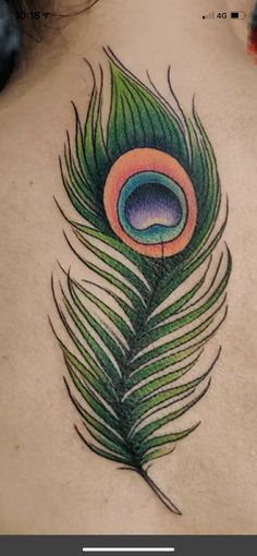 a peacock feather tattoo on the back of a woman's shoulder