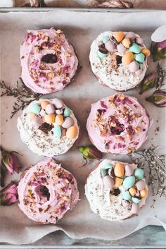 four cakes decorated with pink frosting and candy eggs on top of each one, surrounded by flowers