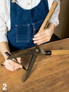 a person holding a large pair of scissors on top of a wooden table with the number 2 in front of them