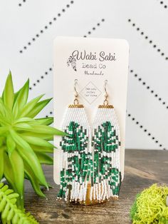 a pair of green and white beaded earrings sitting on top of a wooden table