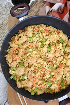 a pan filled with rice and vegetables on top of a wooden cutting board next to utensils