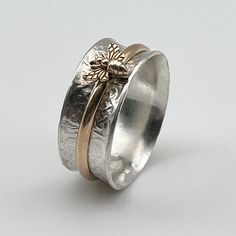 This ring is made in our Ohio Studio just for you at time of order. You will love the feel of the wide band and spinning the Bee around. The main band is made with solid sterling silver. The tiny bronze Bee is mounted on a 14/20 gold filled band.  Available in various sizes from 6 to 10 and 1/2 sizes. If you need a 1/4 size just message us. Great gift mode! Free exchanges if you inadvertently order wrong size. Thank you for looking at our shop! Adjustable Double Band Gift Bands, Adjustable Thick Band Gift Bands, Adjustable Thick Band For Gift, Adjustable Thick Band Wide Ring As Gift, Adjustable Thick Band Wide Ring Gift, Stamped Wide Band Jewelry Gift, Stamped Wide Band Jewelry For Gift, Anniversary Jewelry With Wide Band And Stamped Details, Gift Jewelry With Stamped Wide Band