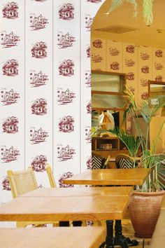 a restaurant with wooden tables and chairs in front of a wallpapered kitchen area