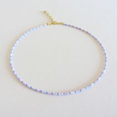 a white beaded necklace with blue beads on a gold plated chain is shown