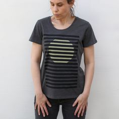 Our Bright Spot t-shirt offers a minimalist, modern take on a rising sun. Inspired by the clean lines and bold colors of the bauhaus movement, it features the heavy black stripes of window blinds in jet black with a pale yellow sun peaking through. We'll call it a cautiously optimistic shirt for these strange times. These women's tees are made in the USA, and have a classic scoop neck silhouette. They're constructed from an eco-friendly 50/50 blend of organic cotton and recycled polyester, and h Modern Fitted T-shirt With Graphic Print, Casual Geometric Tops For Spring, Modern Graphic Design Tops With Relaxed Fit, Modern Cotton Tops With Screen Print, Modern Crew Neck Top With Screen Print, Modern Crew Neck Tops With Graphic Design, Modern Graphic Design Crew Neck Tops, Modern Relaxed Fit Shirt, Cautiously Optimistic