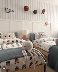 two beds in a bedroom with blue and white wallpaper, one has a stuffed animal on the bed