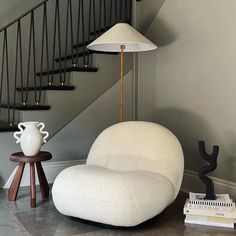 a white chair sitting under a stair case next to a lamp