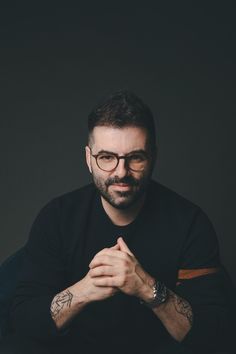 a man with glasses sitting in front of a black background and looking at the camera