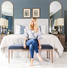 a woman sitting on top of a bench in front of a bed with blue walls