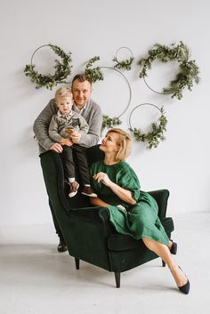 a man, woman and child sitting on a green chair in front of a wall with wreaths