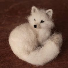 a small white stuffed animal sitting on top of a wooden table next to a brown surface