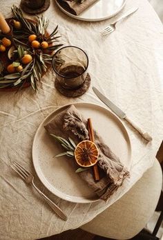 the table is set with plates, silverware and an orange slice on top of it