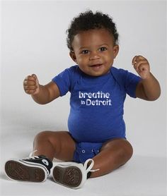 a baby sitting on the floor with his hands up and smiling at the camera while wearing a blue shirt