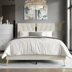 a white bed sitting in a bedroom next to a dresser and window with a chandelier hanging above it