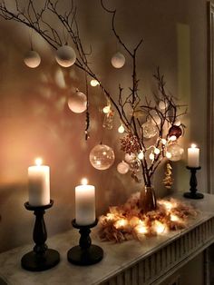 some candles are sitting on a mantle in front of a tree with balls and branches