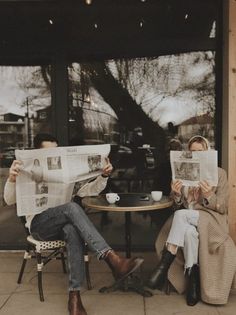 two people sitting at a table reading newspapers