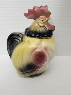 a ceramic rooster is sitting on top of it's head and has its eyes closed