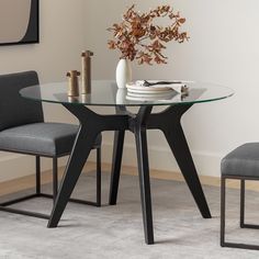 a glass table with two chairs and a vase on top of it in front of a white wall