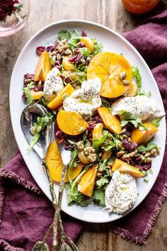 a white plate topped with salad next to a glass of orange juice and two silver spoons