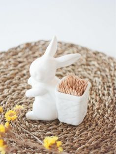 a white rabbit figurine sitting next to a cup filled with flowers on top of a woven place mat